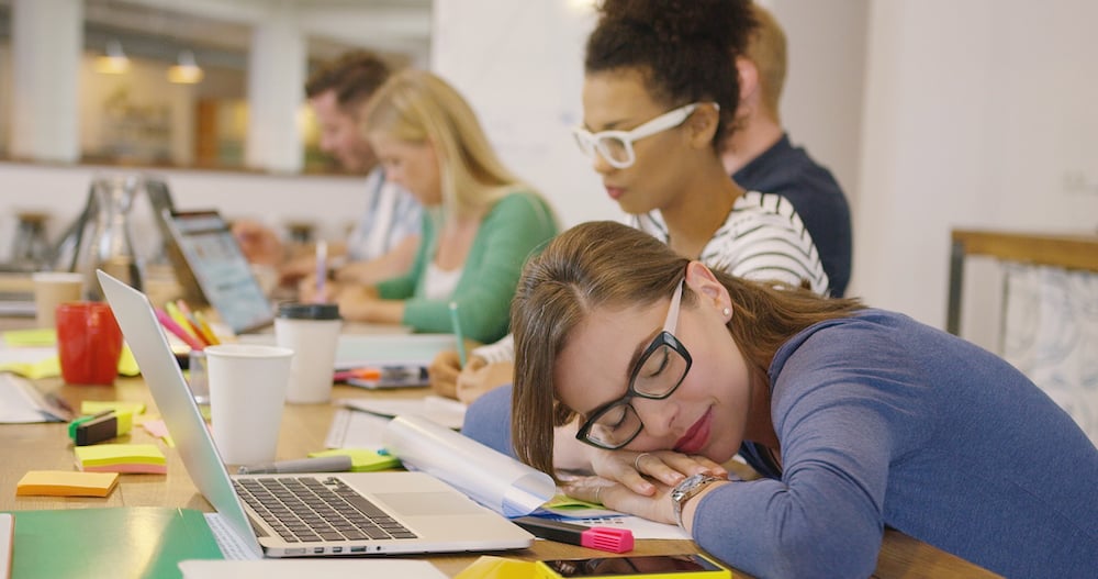 employee-sleeping-at-table-with-coworkers-PDT2LGA