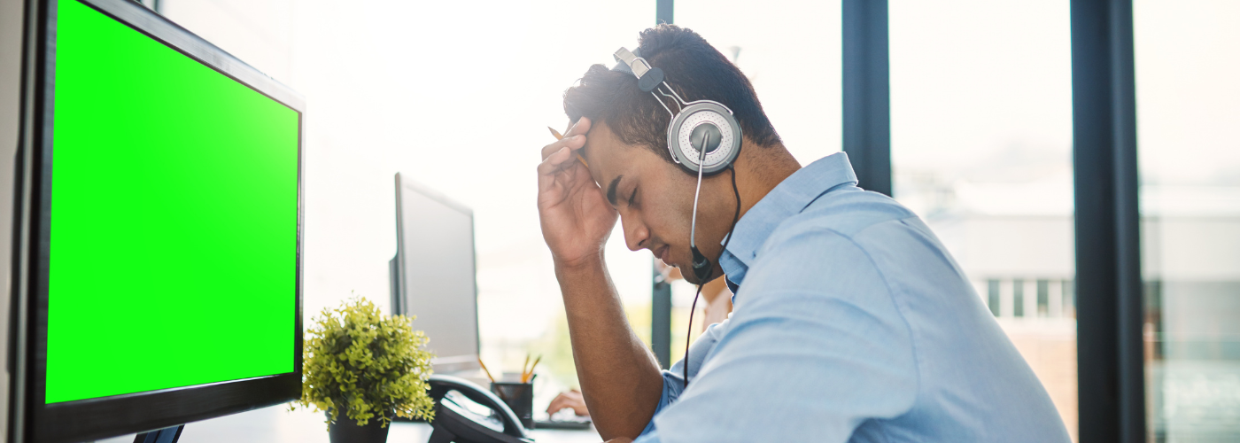A young male with a hard time focusing with headphones on sitting at his desk in front of a big green computer screen.